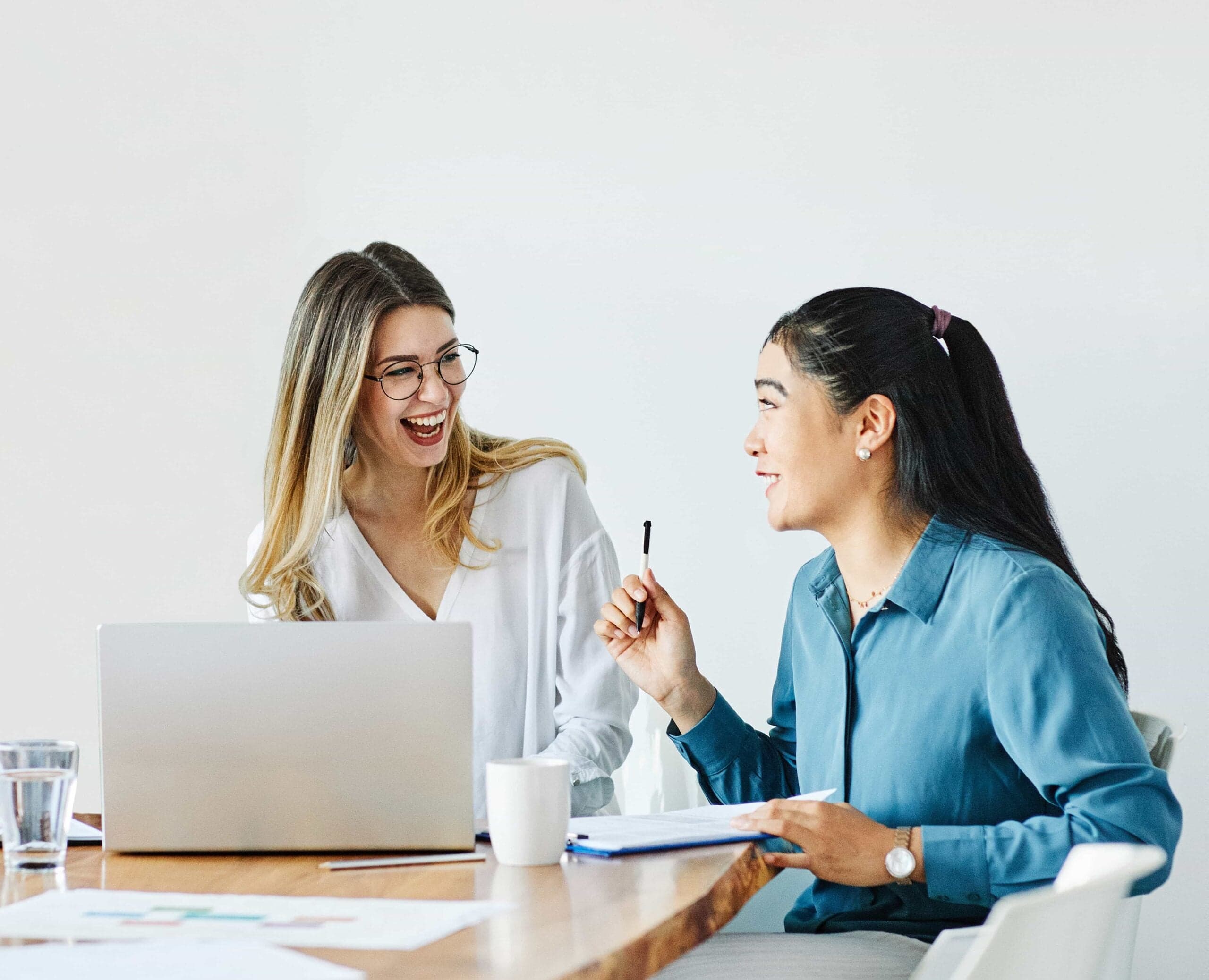 How to Give Feedback to Manager: 10 Scripts & Proven Tips 1 Two professional women collaborating and laughing during a business meeting with a laptop with documents on a desk and give feedback to manager in Denver, CO.