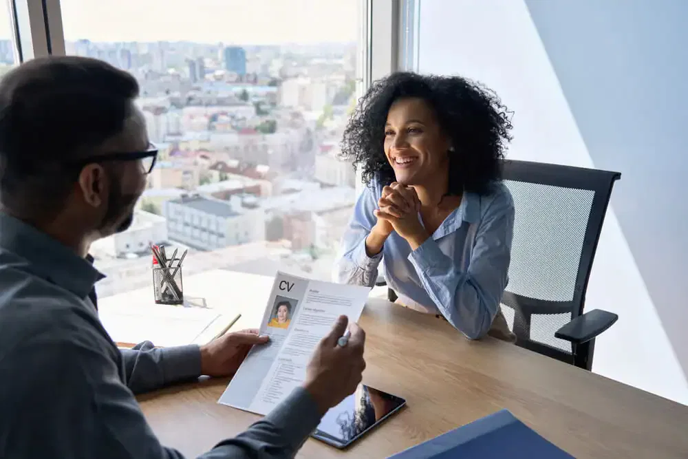 A professional job interview at a high-end Ocala hotel featuring a smiling female candidate with curly hair and a male recruiter holding a CV in a modern office with a city view.