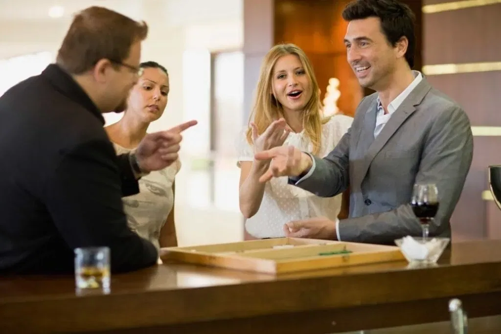 Friends laughing and playing a competitive game of backgammon at an upscale hotel bar with craft drinks in Los Angeles, California.